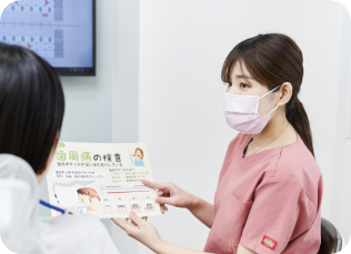 歯科衛生士が歯周病のパンフレットを使い、患者に口腔ケアの重要性を説明しているカウンセリング風景